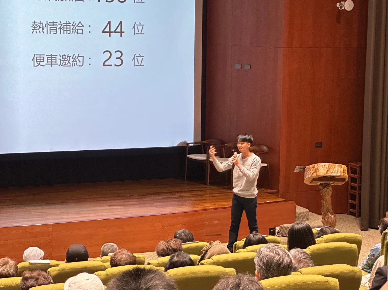 簡報投影出「熱情補給：44 位」「便車邀約：23 位」，講者在台前拿著麥克風說明