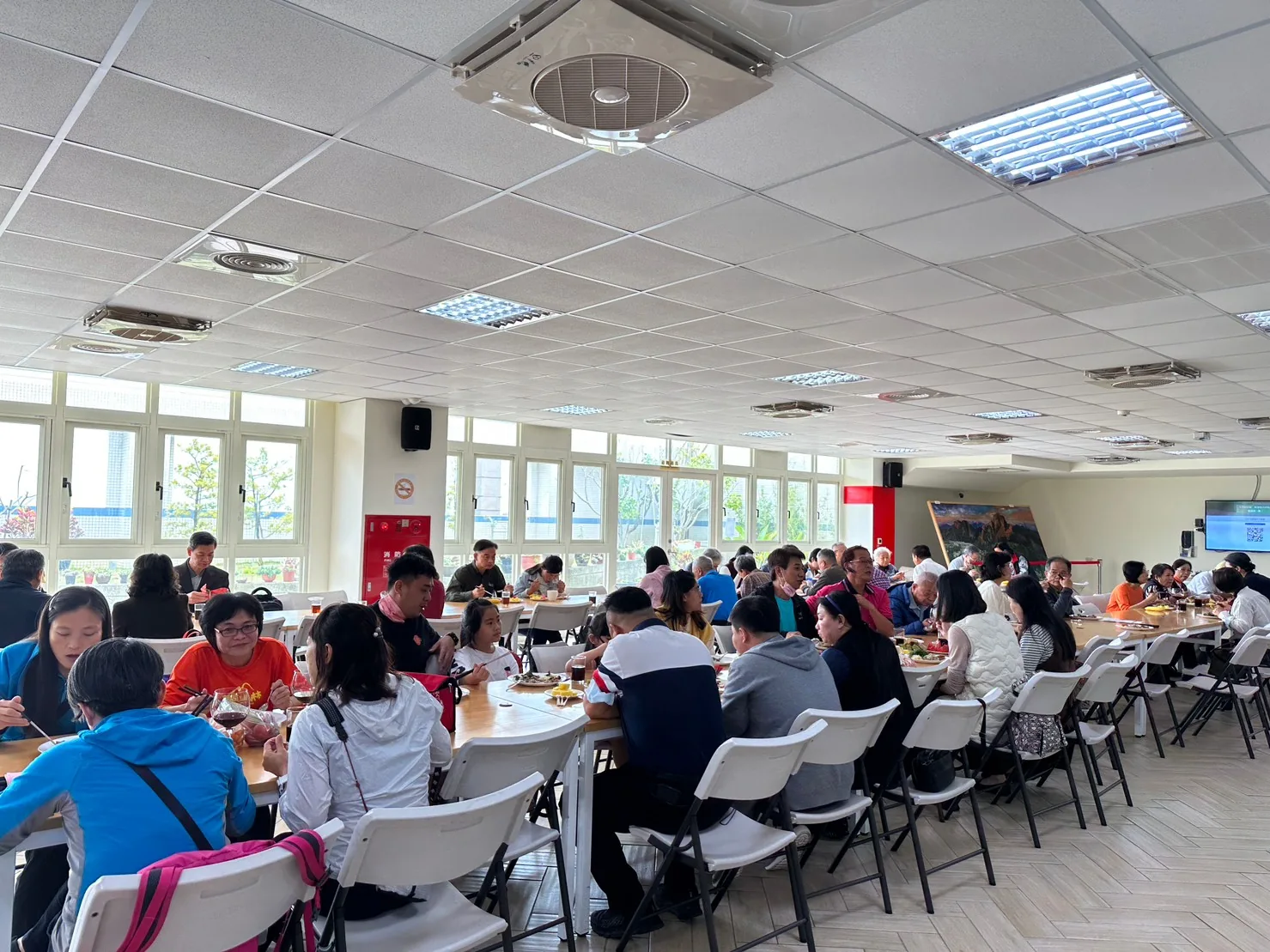餐廳長桌並排，參加者分坐兩側用餐，遠景廣角